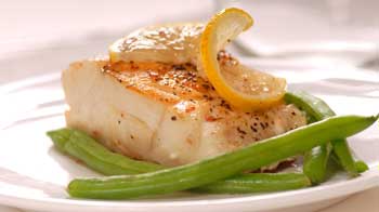 A photograph of pan roasted paiche with herbs and lemon juice served with green beans.